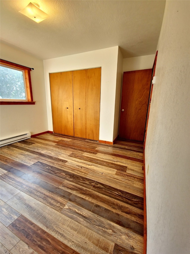 unfurnished bedroom featuring a textured ceiling, a baseboard radiator, a closet, and hardwood / wood-style flooring