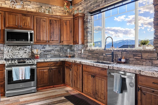 kitchen with light wood-type flooring, stainless steel appliances, a mountain view, sink, and tasteful backsplash