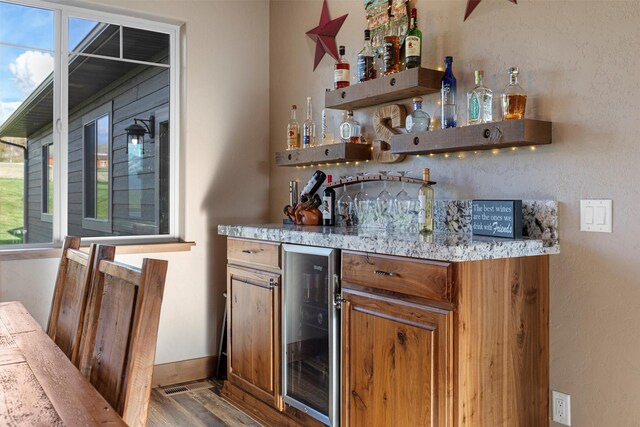 bar with beverage cooler, light stone countertops, a wealth of natural light, and dark wood-type flooring