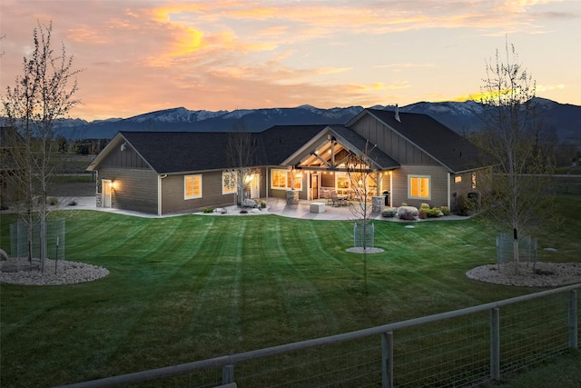 back house at dusk with a mountain view, a yard, and a patio area