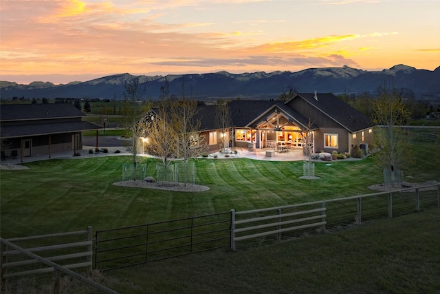 back house at dusk featuring a yard, a mountain view, a patio area, and a rural view