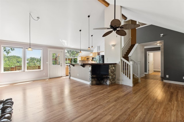 unfurnished living room with high vaulted ceiling, baseboards, stairs, light wood finished floors, and beamed ceiling