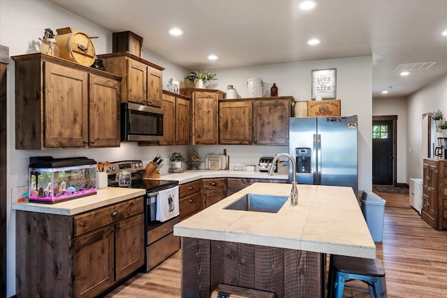 kitchen featuring sink, a breakfast bar area, light hardwood / wood-style flooring, appliances with stainless steel finishes, and an island with sink