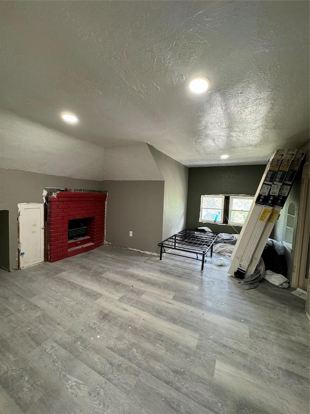 unfurnished living room with a textured ceiling, wood-type flooring, lofted ceiling, and a fireplace