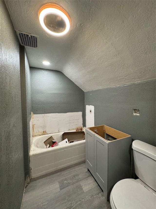 bathroom with hardwood / wood-style floors, toilet, lofted ceiling, and a textured ceiling