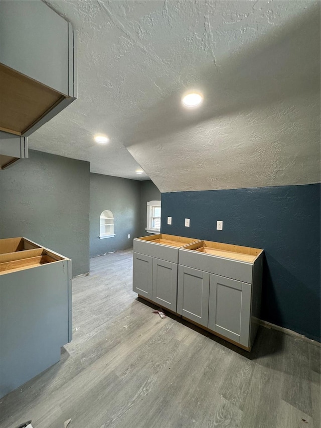 interior space featuring light wood-type flooring, a textured ceiling, and vaulted ceiling