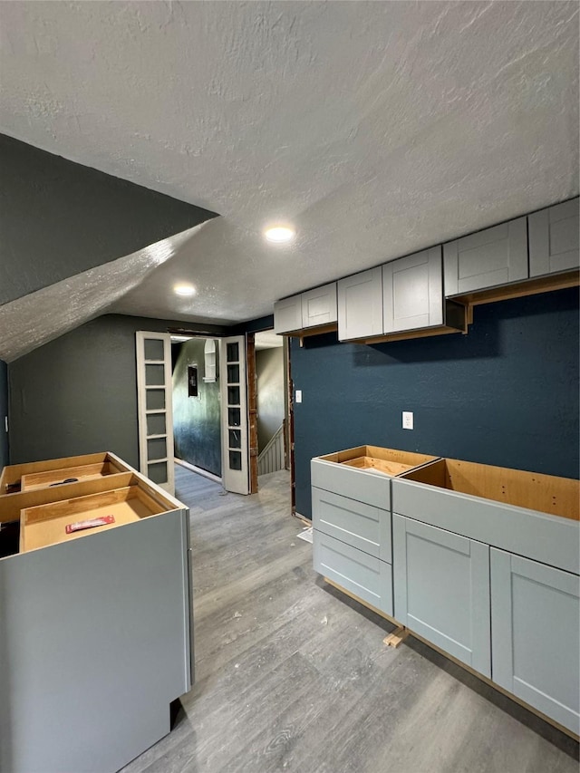 kitchen with lofted ceiling, light hardwood / wood-style floors, white cabinetry, and a textured ceiling