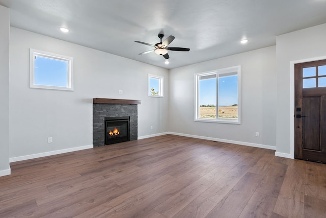 unfurnished living room with wood-type flooring, ceiling fan, and a stone fireplace