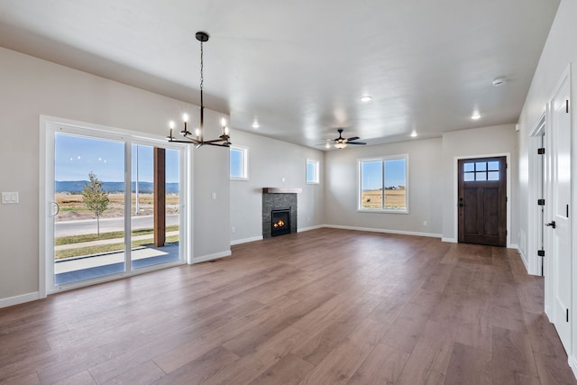 unfurnished living room with ceiling fan with notable chandelier, wood-type flooring, a mountain view, and a fireplace