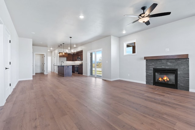 unfurnished living room featuring ceiling fan, a stone fireplace, hardwood / wood-style flooring, and sink