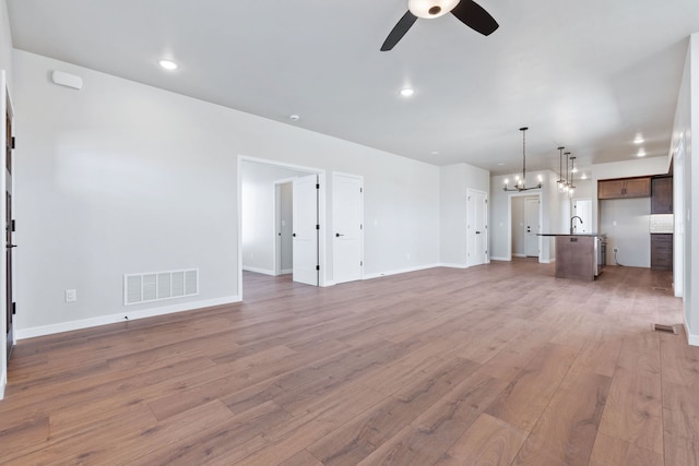 unfurnished living room with ceiling fan with notable chandelier, sink, and hardwood / wood-style flooring