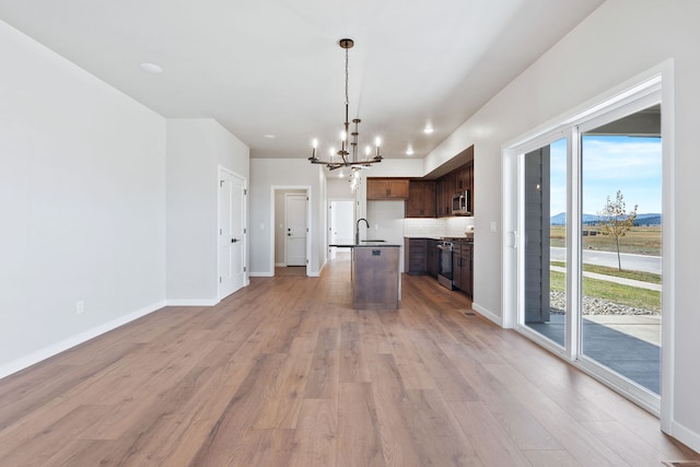 kitchen with light wood-type flooring, a healthy amount of sunlight, a center island with sink, and stainless steel appliances