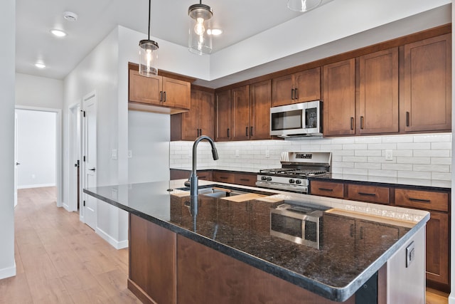 kitchen featuring light hardwood / wood-style floors, an island with sink, stainless steel appliances, dark stone counters, and sink