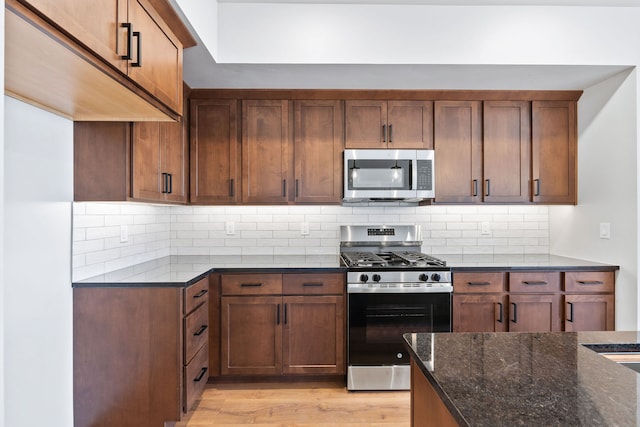 kitchen featuring dark stone counters, light wood-type flooring, decorative backsplash, and appliances with stainless steel finishes