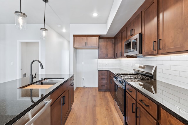 kitchen featuring appliances with stainless steel finishes, decorative backsplash, light hardwood / wood-style floors, pendant lighting, and sink