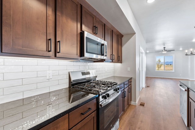 kitchen with appliances with stainless steel finishes, decorative backsplash, light wood-type flooring, ceiling fan, and dark stone counters