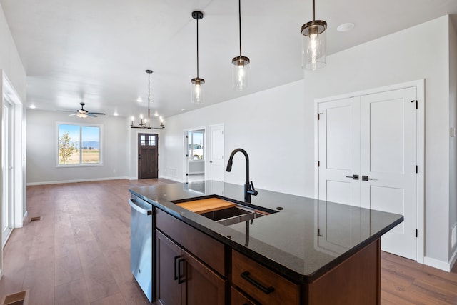 kitchen featuring an island with sink, sink, decorative light fixtures, dark stone counters, and dark hardwood / wood-style flooring