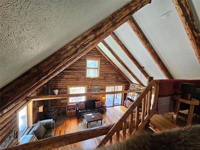 interior space with a wood stove, wooden walls, a textured ceiling, wood-type flooring, and vaulted ceiling