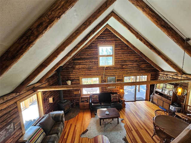 living room with a wood stove, wooden walls, beamed ceiling, hardwood / wood-style floors, and plenty of natural light