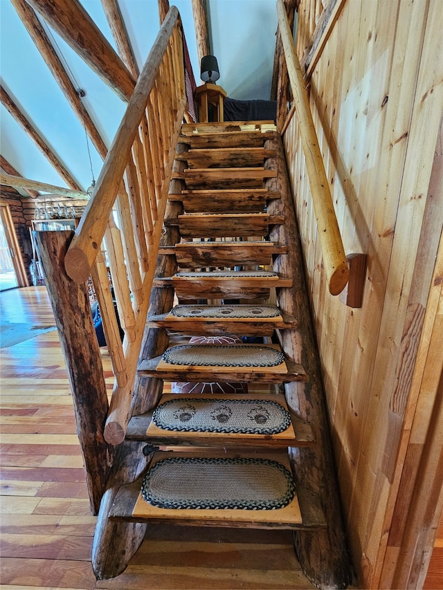 stairway featuring lofted ceiling with beams, wooden walls, and hardwood / wood-style flooring