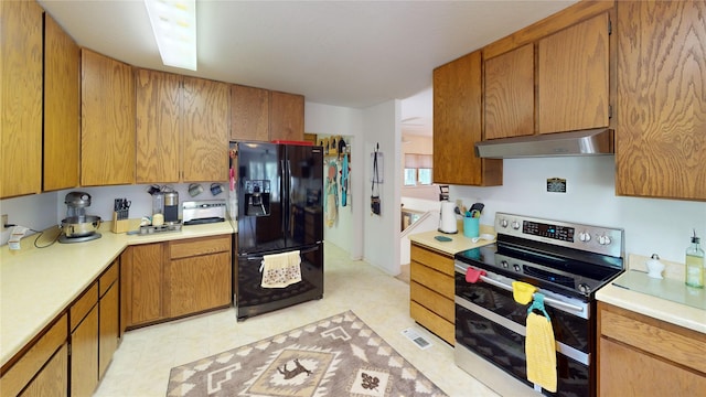 kitchen featuring light countertops, black fridge, under cabinet range hood, brown cabinetry, and range with two ovens