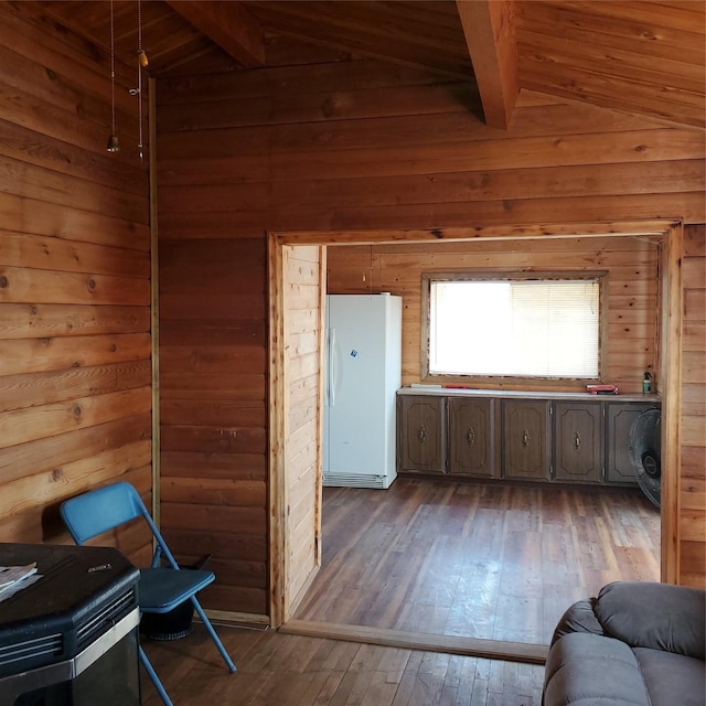 interior space featuring freestanding refrigerator, wood walls, hardwood / wood-style flooring, and vaulted ceiling with beams