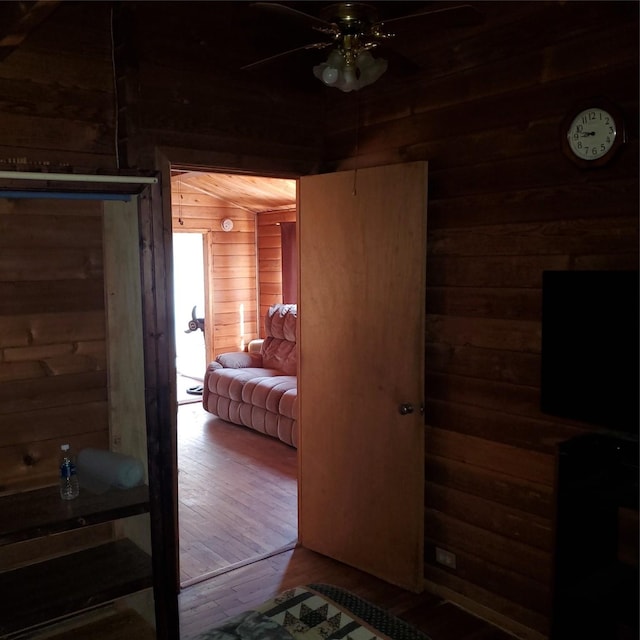 bedroom with wood-type flooring, wood walls, and ceiling fan