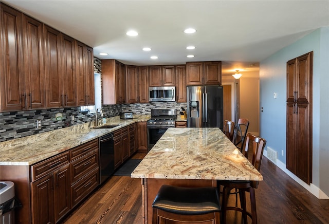 kitchen featuring dark wood-style flooring, light stone countertops, a sink, stainless steel appliances, and decorative backsplash