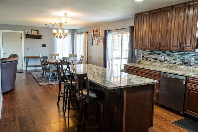 kitchen featuring stainless steel dishwasher, a chandelier, dark wood-style floors, and a kitchen bar