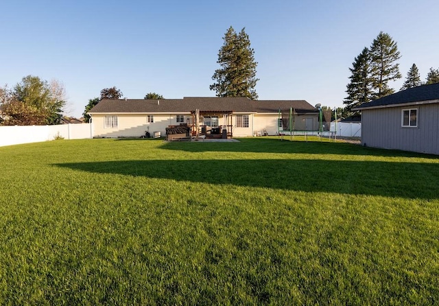 back of property with fence, a trampoline, and a yard