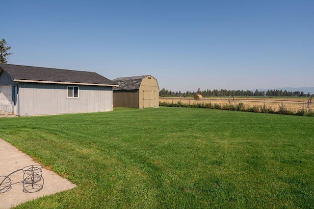 view of yard with a rural view, fence, an outdoor structure, and a storage unit