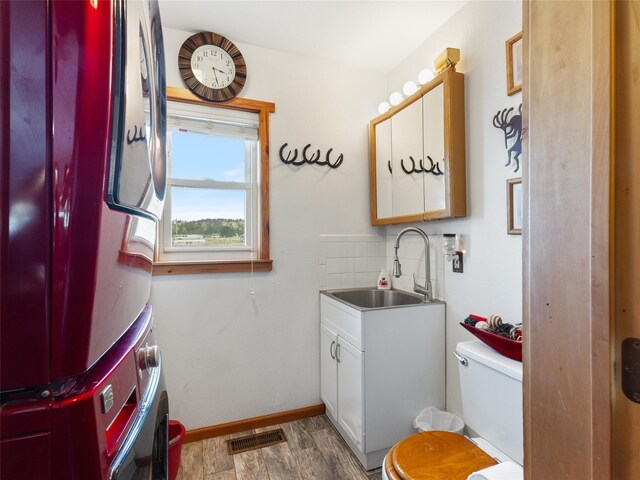 bathroom with decorative backsplash, toilet, stacked washer / drying machine, vanity, and hardwood / wood-style flooring