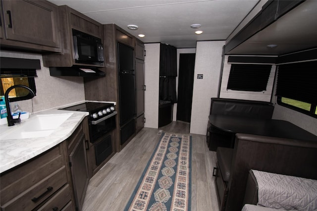 kitchen featuring dark brown cabinets, sink, light wood-type flooring, and black microwave