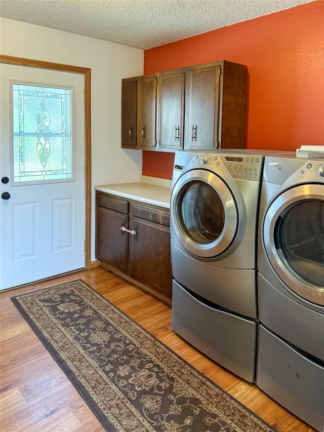 laundry room featuring cabinet space, light wood finished floors, a textured ceiling, and washing machine and clothes dryer