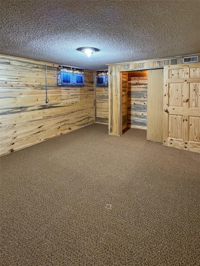 finished basement with wood walls, a textured ceiling, visible vents, and carpet flooring