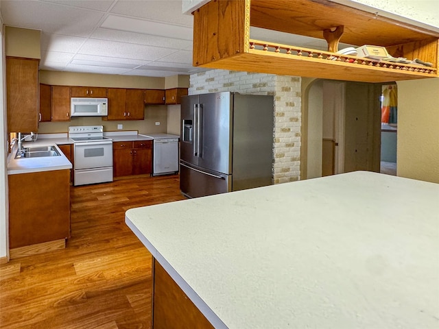 kitchen featuring white appliances, a sink, light countertops, brown cabinets, and dark wood-style floors