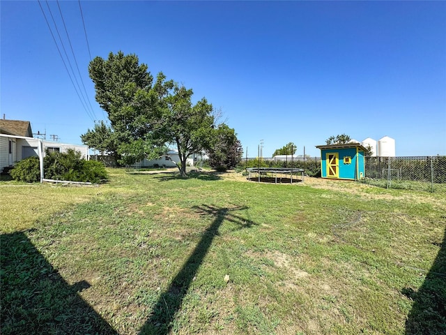 view of yard featuring a trampoline, an outbuilding, fence, and a storage shed