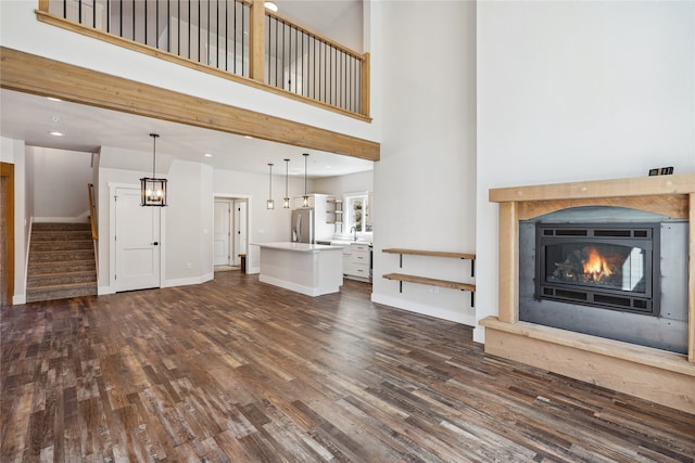 unfurnished living room with an inviting chandelier, dark hardwood / wood-style floors, and a towering ceiling