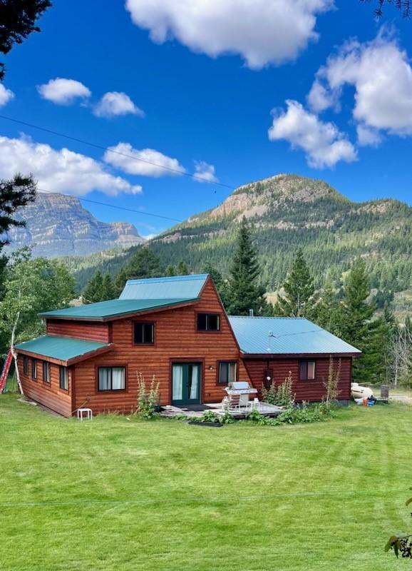 rear view of house with a yard, a view of trees, metal roof, and a mountain view