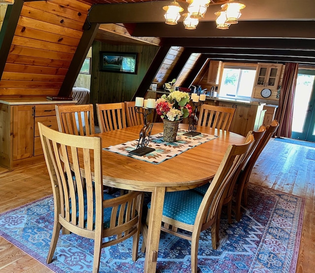 dining area featuring wood walls, wood-type flooring, a chandelier, and beam ceiling