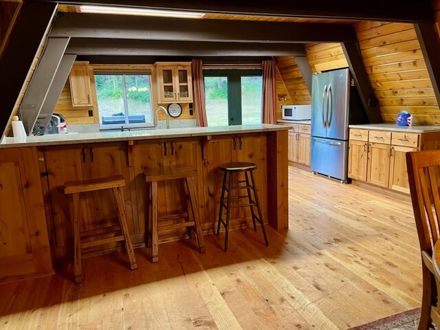 kitchen with kitchen peninsula, wooden walls, light hardwood / wood-style floors, and stainless steel refrigerator