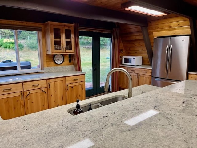 kitchen with light stone counters, a sink, french doors, white microwave, and freestanding refrigerator