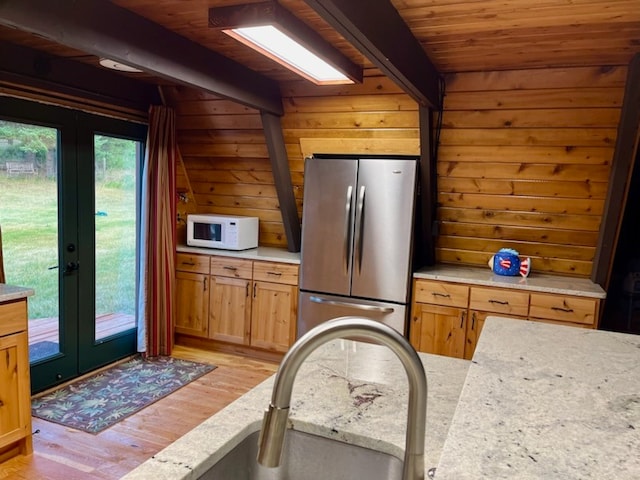 kitchen with wood ceiling, wooden walls, light hardwood / wood-style floors, and stainless steel refrigerator