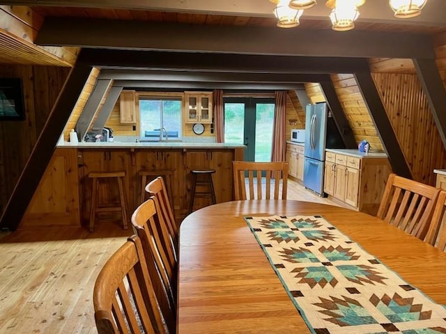 dining room with vaulted ceiling with beams, light wood-style flooring, wooden walls, and wooden ceiling
