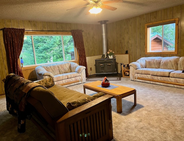 carpeted living room featuring wooden walls, ceiling fan, a wood stove, and a textured ceiling