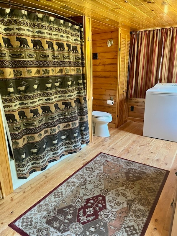 bathroom with toilet, wooden walls, wood ceiling, hardwood / wood-style flooring, and washer / clothes dryer