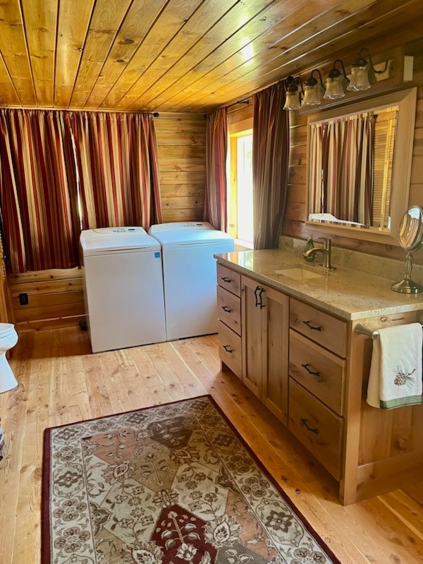 bathroom with toilet, vanity, wood walls, washing machine and dryer, and hardwood / wood-style flooring