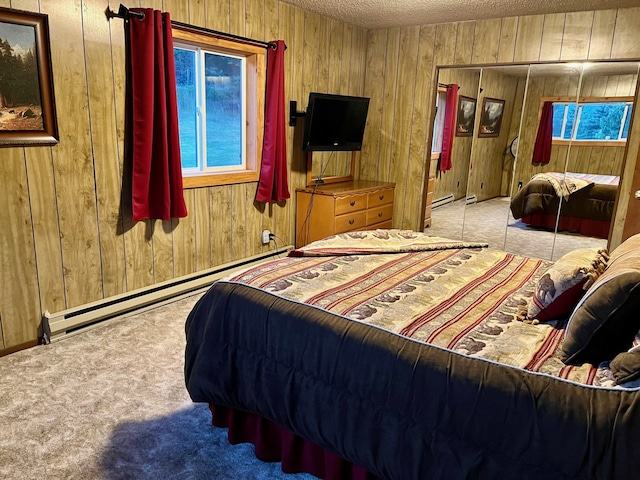 carpeted bedroom with baseboard heating, a textured ceiling, wooden walls, and a closet