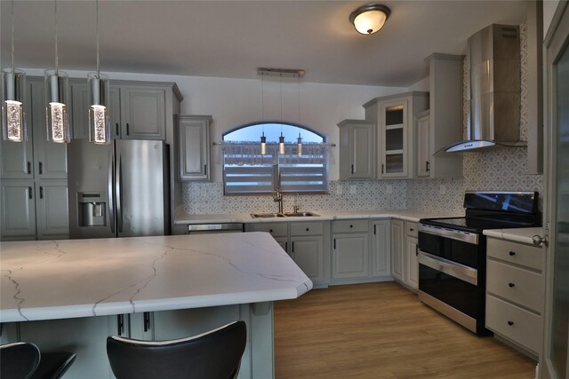 kitchen featuring wall chimney exhaust hood, gray cabinetry, hanging light fixtures, a kitchen breakfast bar, and stainless steel appliances