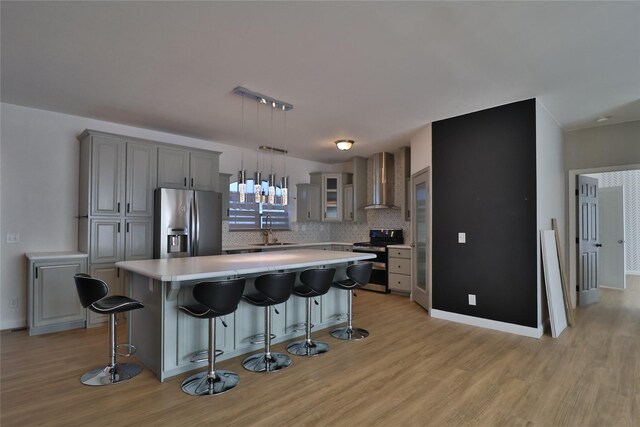 kitchen featuring a kitchen island, sink, gray cabinetry, stainless steel appliances, and wall chimney exhaust hood